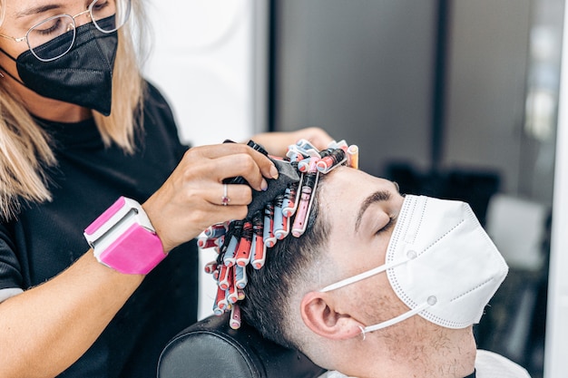 Profile of a hairdresser applying applying hair dye to a young caucasian man in a salon