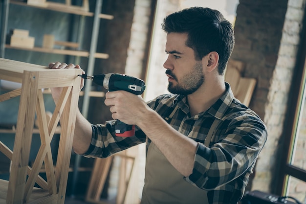 Photo profile  handsome guy building book shelf handmade design assembling using drill wooden industry home woodwork workshop indoors