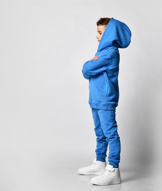 Profile of a little brunette boy in blue sportswear and white sneakers