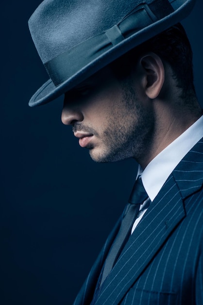 Профиль мафиози в костюме и фетровой шляпе на темном фоне