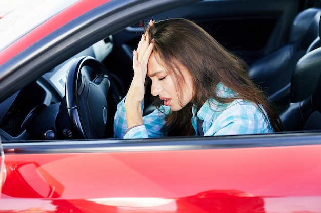 profile of nervous woman driving red car, stress while driving. tensed woman leaning on hand with closed eyes, traffic jams. head and shoulders of brunette woman inside car