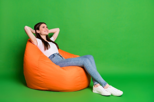 Profile photo of adorable cheerful young lady hold hands behind head dress white t-shirt jeans footwear isolated on green background