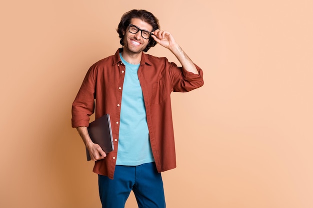 Foto la foto del profilo di un uomo allegro tiene un sorriso a trentadue denti da netbook indossa occhiali t-shirt marrone sfondo di colore beige isolato