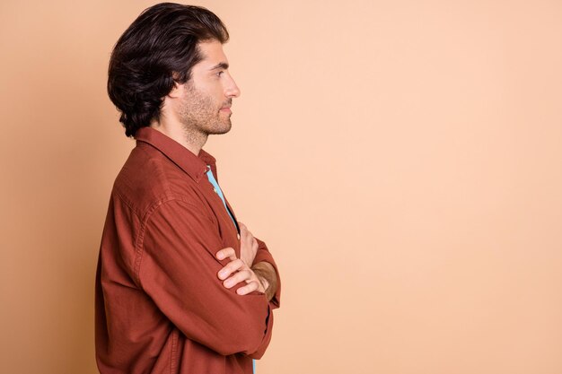 Profile photo of confident young man crossed hands look empty space wear brown t-shirt isolated beige color background