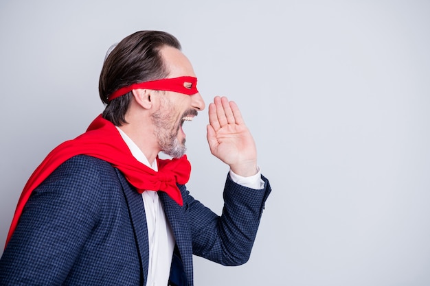 Profile photo of crazy yelling aged mature business guy super hero costume look scream novelty information empty space arm near mouth wear suit red face mask cloak isolated grey background