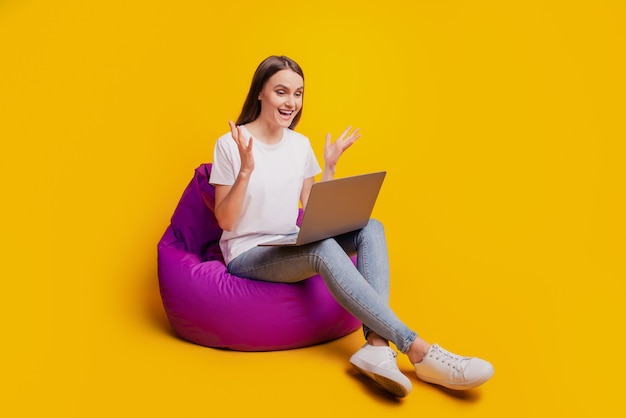 Фотография профиля возбужденной дамы, сидящей на мешочке на работе, на удаленном компьютере, в белой футболке, позирующей на желтом фоне