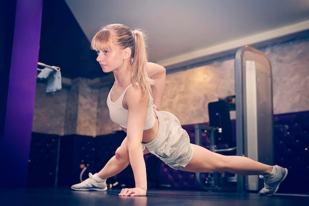 Profile photo focused powerful strong beautiful charming enduring woman with blonde hair and ponytail hairdo standing on hands doing plank and pushups gym club
