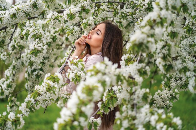 Profile photo of a girl with long dark hair against the backdrop of a blooming garden