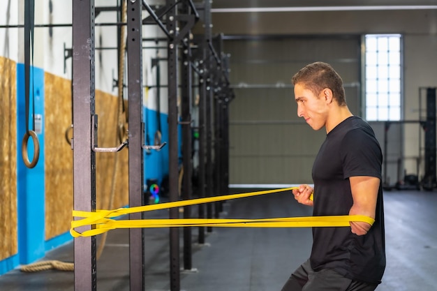 Profile photo of a sportive man with one arm amputated training with elastic bands in a cross training gym