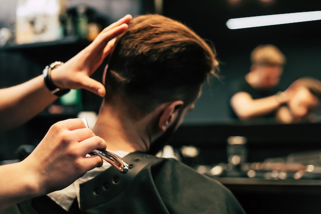 Profile photo of a young barber trimming his customerÃ¢ÂÂs hair with an electric shaver and a comb in a barbershop.