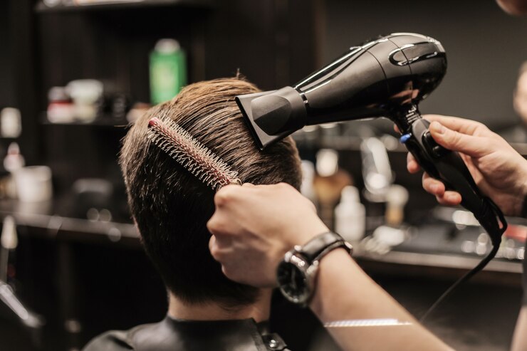Photo profile photo of a young barber trimming his customerã¢ââs hair with an electric shaver and a comb in a barbershop.