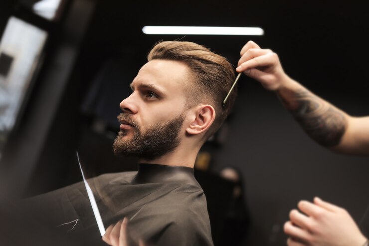 Photo profile photo of a young barber trimming his customerã¢ââs hair with an electric shaver and a comb in a barbershop.