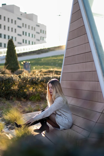 Профильная фотография красивой молодой блондинки, сидящей рядом с современным зданием