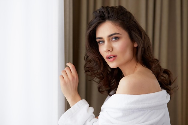 Profile portrait of a beautiful brunette young woman with hairstyle in a white bathrobe