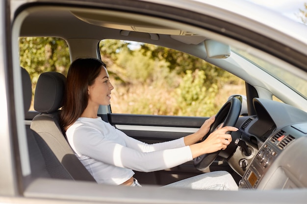 一人で車に乗って満足している幸せな肯定的な表情で喜んで満足している美しい女性の横顔の肖像画は、肯定的な表情で道路を見て運転席に座っています