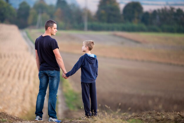 Profile portrait of father and son standing in grassy field holding hands