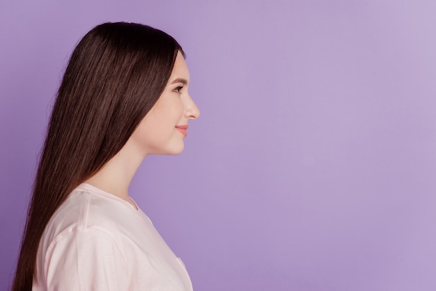 Profile portrait of happy charming adorable girl look empty space posing on purple wall