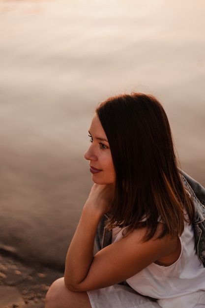 Profile portrait of a pretty young woman in the sunset twilight with the sea surface on the background