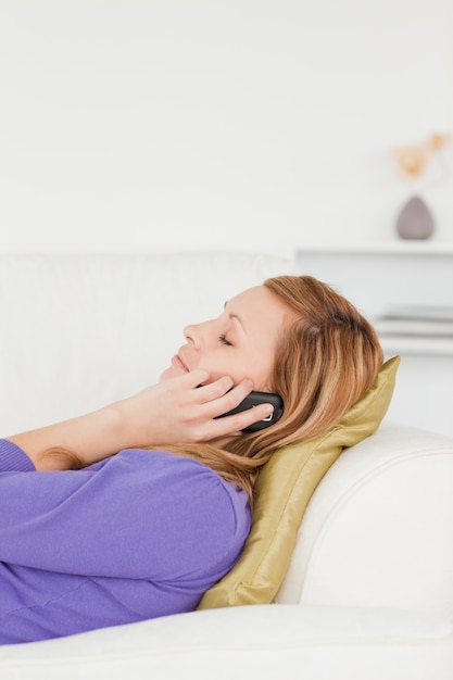 Profile portrait of a serene red-haired woman on phone while lying on a sofa