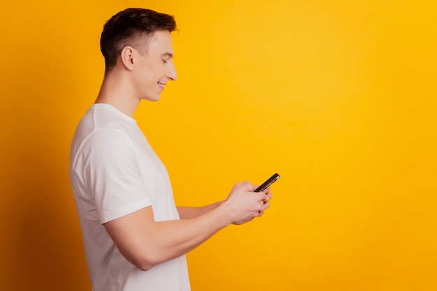 スマートクールな男のプロフィールの肖像画は、黄色の背景に電話ルック画面を保持します