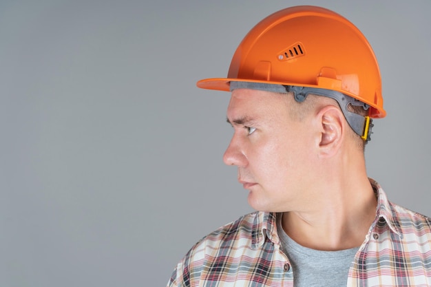 Photo profile portrait of a worker in an orange helmet on a gray background, close-up