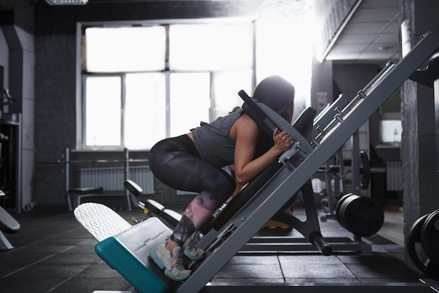 Profile shot of a strong athletic woman doing squats in hack squat gym machine