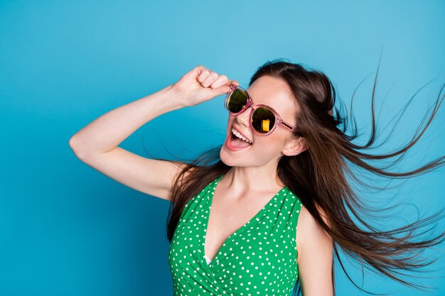 Profile side photo of pretty candid girl touch glasses enjoy rejoice weekend air wind blow hairstyle wear good look clothes isolated over blue color background