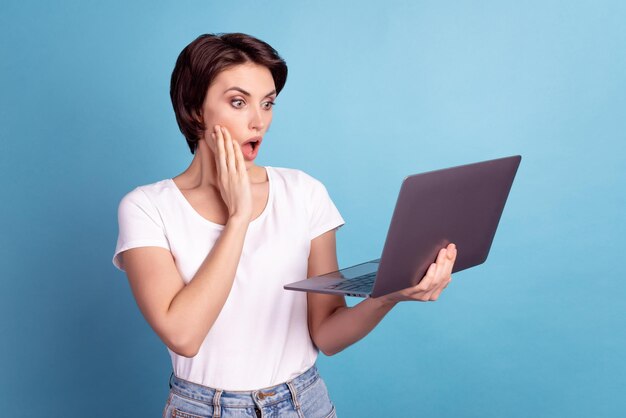 Profile side photo of young woman hand touch cheek shocked face reaction mistake laptop isolated over blue color background.