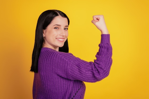 若い女性のプロフィールの側面写真幸せなポジティブな笑顔は、黄色の背景に分離されたスポーティーな手の筋肉を示しています