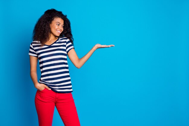 Photo profile side view of cheerful afro american woman promoter holding something, product presentation, copy space on blue wall