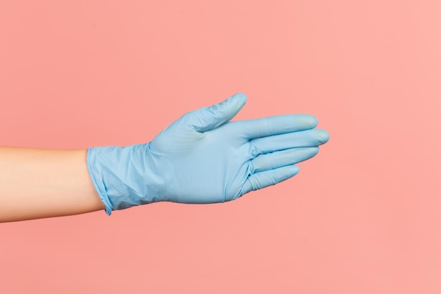 Profile side view closeup of human hand in blue surgical gloves giving hand to greeting or touching.