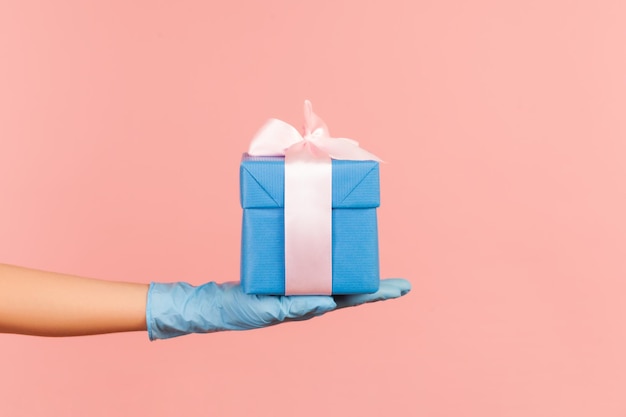 Profile side view closeup of human hand in blue surgical gloves holding blue gift box.