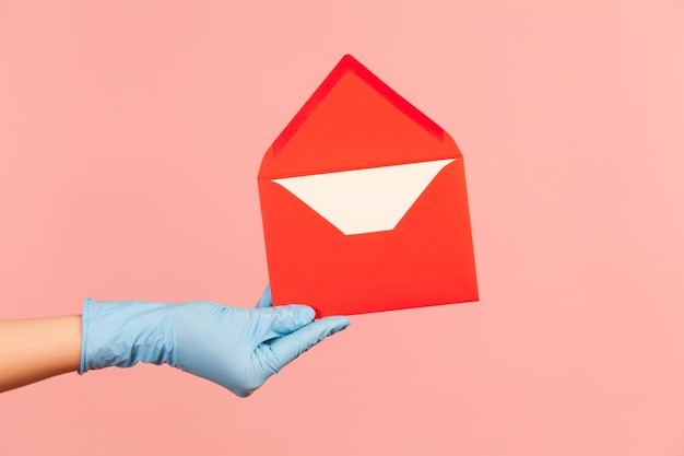 赤い開いた手紙の封筒を保持している青い手術用手袋の人間の手のプロファイルの側面図のクローズアップ。