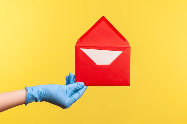 Profile side view closeup of human hand in blue surgical gloves holding red opened letter envelope.