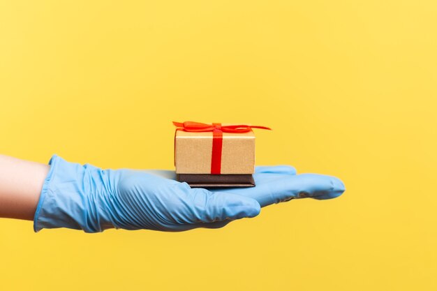 Крупный план взгляда со стороны профиля человеческой руки в синих хирургических перчатках держа небольшую подарочную коробку.