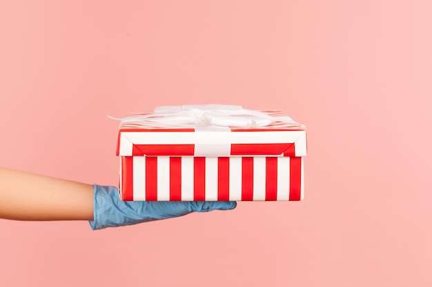 Profile side view closeup of human hand in blue surgical gloves holding striped red white gift box.