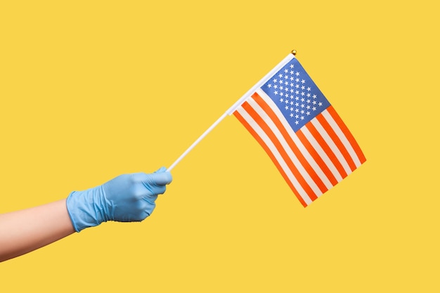 Profile side view closeup of human hand in blue surgical gloves holding USA national flag.