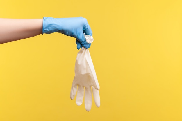 Profile side view closeup of human hand in blue surgical gloves holding white gloves