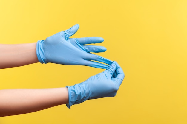 Profile side view closeup of human hand in blue surgical gloves\
showing how to take of gloves.