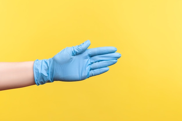 파란색 수술용 장갑을 끼고 인사하거나 만지는 사람의 손을 클로즈업하는 프로필 측면.