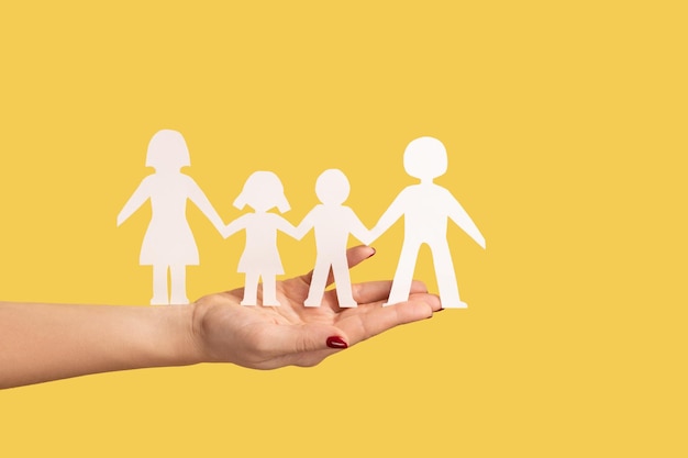 Profile side view closeup of woman hand holding paper family chain relationships between children and parents Indoor studio shot isolated on yellow background