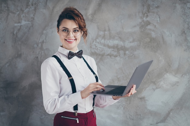 Profilo vista laterale ritratto di lei bella attraente piuttosto contenuto allegra ragazza dai capelli ondulati allegra utilizzando il computer portatile che lavora a distanza autosviluppo isolato su sfondo grigio muro industriale di cemento