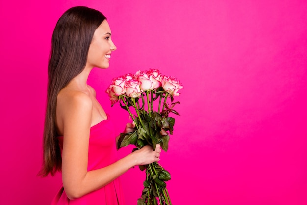 Profile side view portrait of her she nice-looking attractive\
lovely cheerful cheery long-haired girl holding in hands cute\
bouquet isolated on bright vivid shine vibrant pink fuchsia color\
background