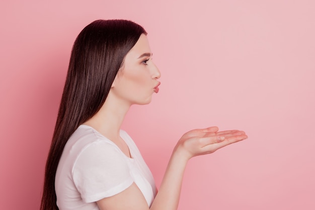 Profile side view portrait of sweet attractive lovely pretty girl sending air kiss empty space isolated over pink background