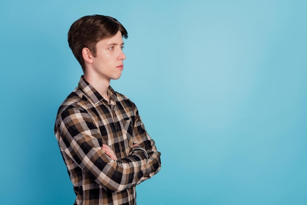 Profile side view portrait of young guy concentrated crossed hands look empty space isolated over blue color background