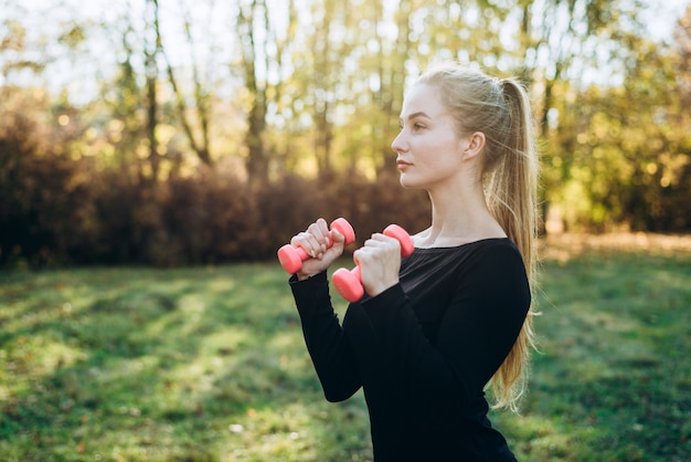 Profile of slim girl with dumbbells outdoors. fitness in park