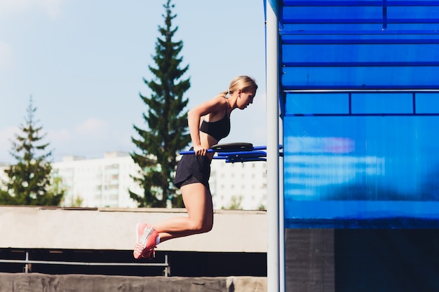 Profile view of female athlete doing some tricep dips on park bench.