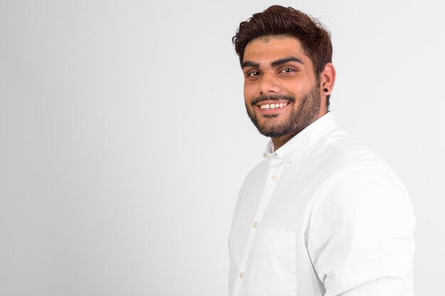 Profile view of happy young bearded Indian man smiling and looking at camera