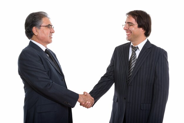 Profile view of happy young and senior Persian businessman smiling and handshaking