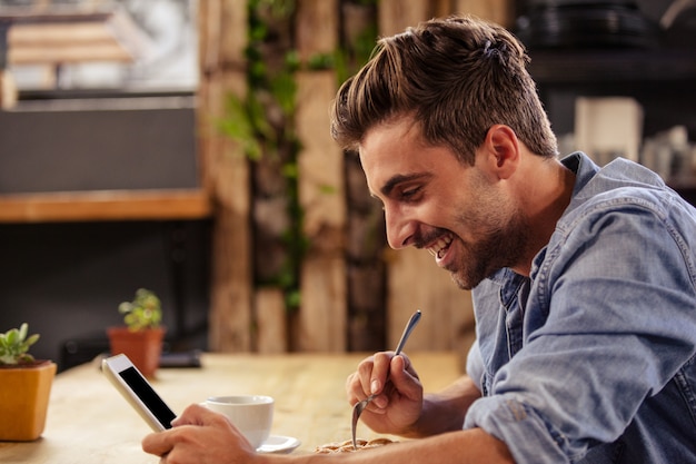 Photo profile view of hipster man using tablet at cafe